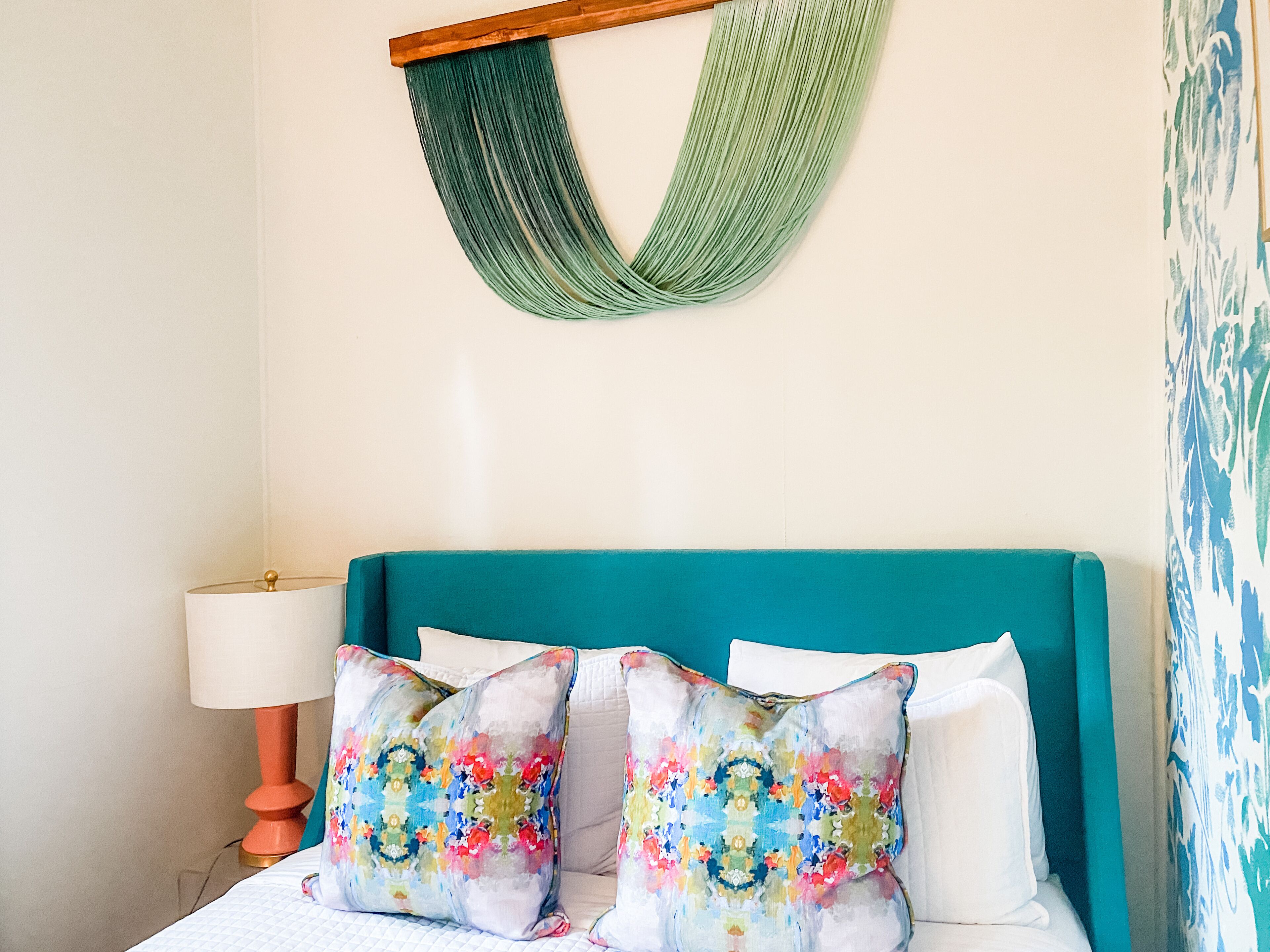 A bed with teal headboard, two colorful pillows, a green hammock, and a bedside lamp.