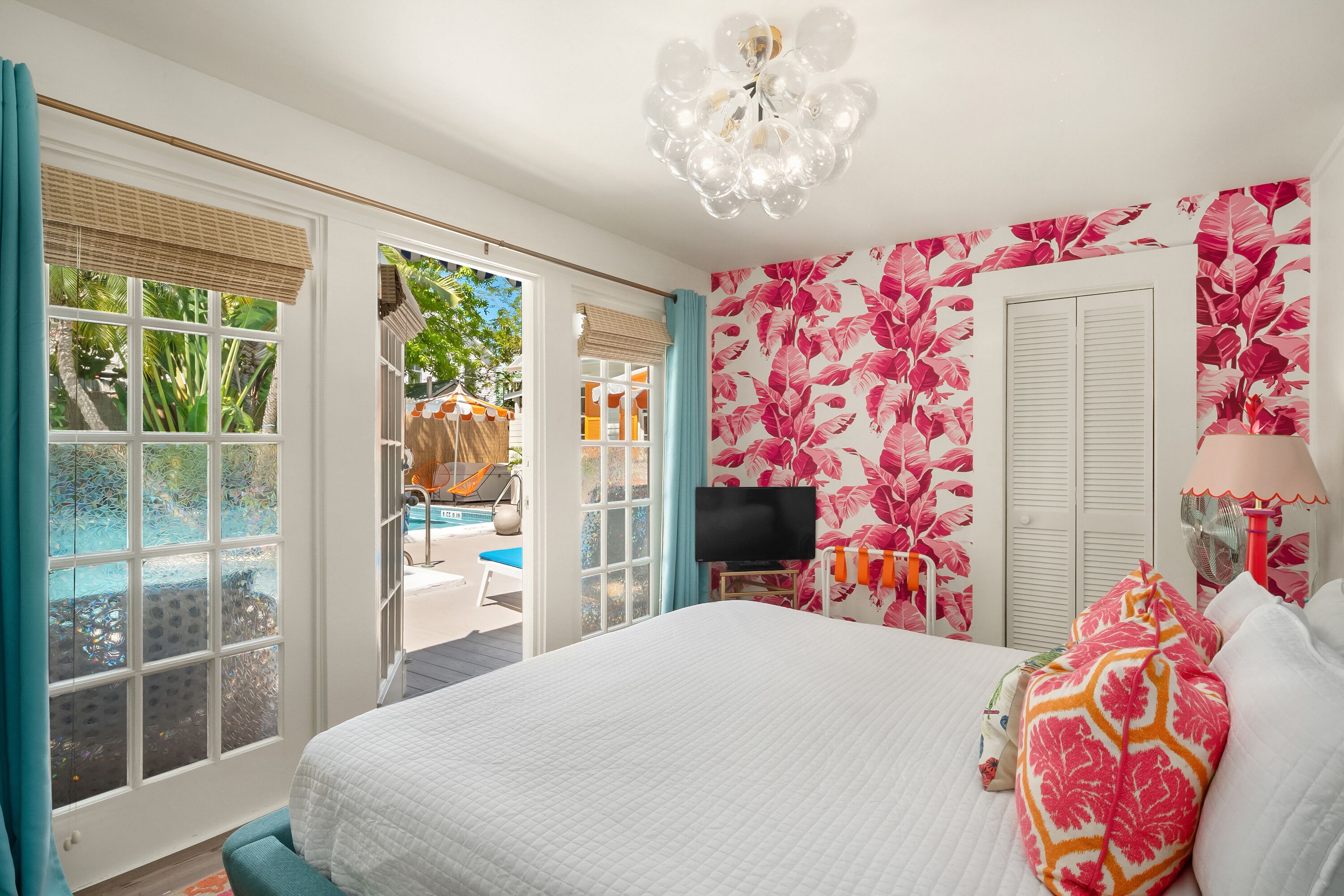 Ein Schlafzimmer mit Bett, Fernseher, Blick auf einen Pool und tropischem Wandpapier.