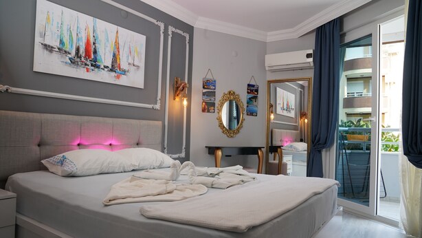 A modern bedroom with a large bed, a painting, a mirror, and a view of the outside balcony. - Alanya Polat Tatil Evleri (Alanya)