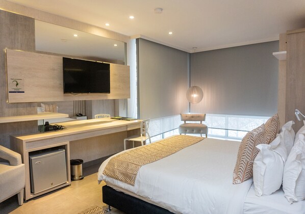 A modern hotel room with a large bed, a desk with a computer, a flat-screen TV, and a small minibar. - Hotel Perla Suite Santa Marta (Santa Marta)
