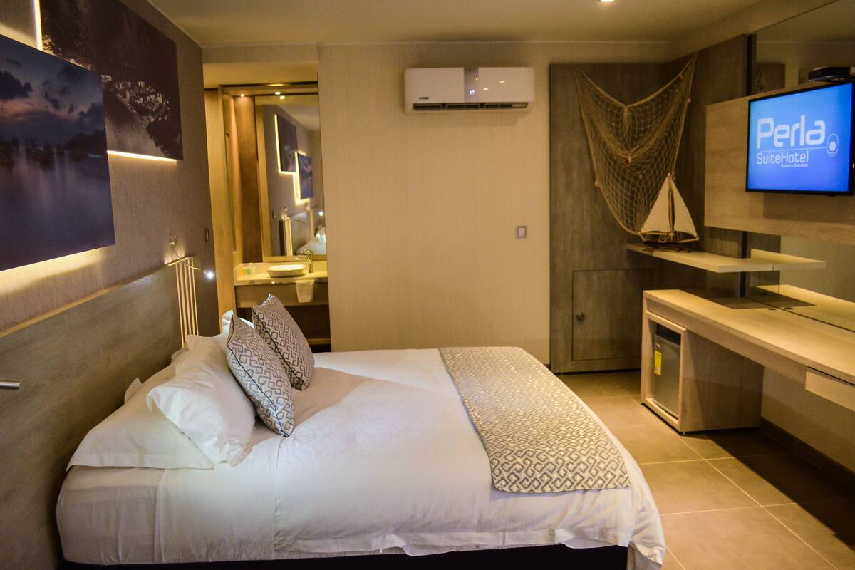 A hotel room with a bed, a TV, a minibar, and a bathroom visible through an open door.