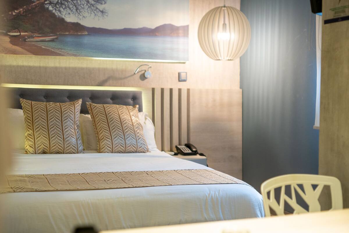 A neatly made bed with patterned pillows, a bedside telephone, and a wall-mounted lamp.