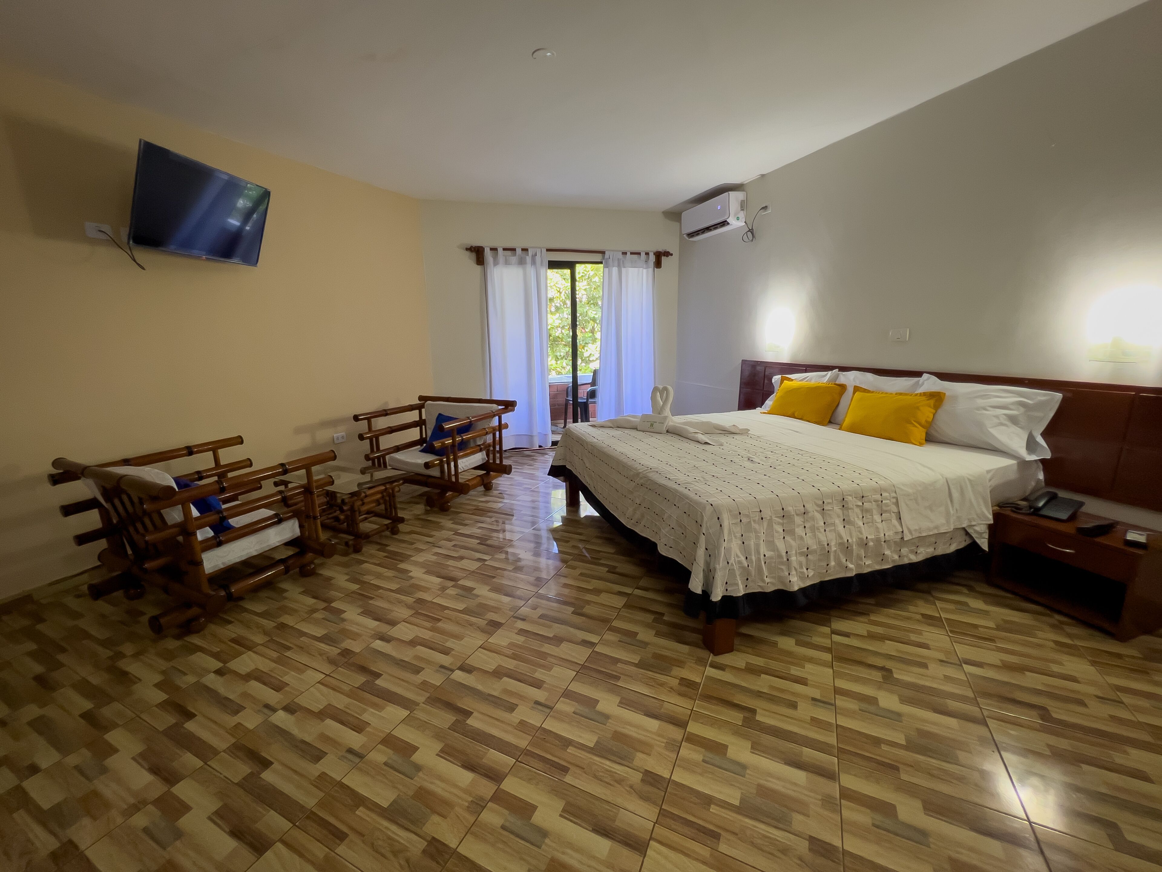 Habitación de hotel con cama, mesita de noche, muebles de madera y televisor montado en la pared.