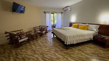 Habitación de hotel con cama, mesita de noche, muebles de madera y televisor montado en la pared.