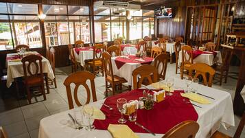 A restaurant with multiple tables set for dining, wooden chairs, and a TV screen mounted on the wall.