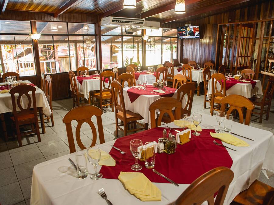 A restaurant with multiple tables set for dining, wooden chairs, and a TV screen mounted on the wall.
