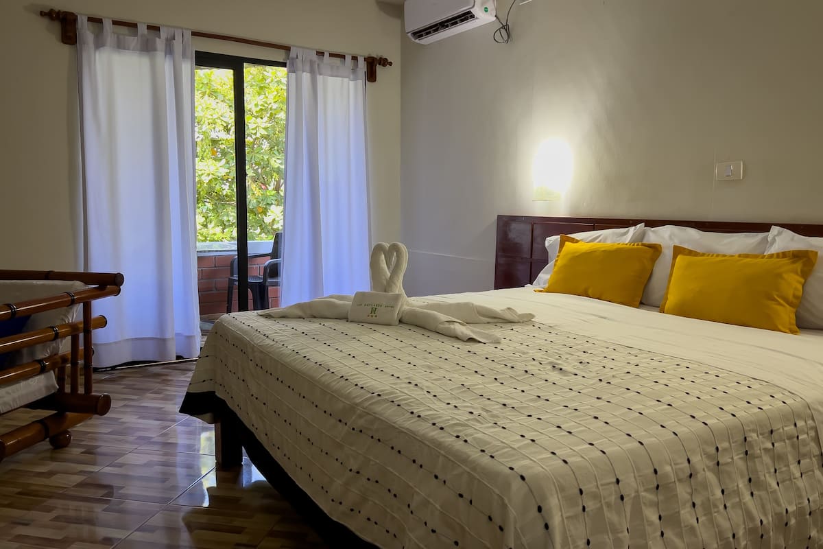 Habitación de hotel con una cama, una silla de madera, una mesa y vistas a zonas verdes por la ventana.