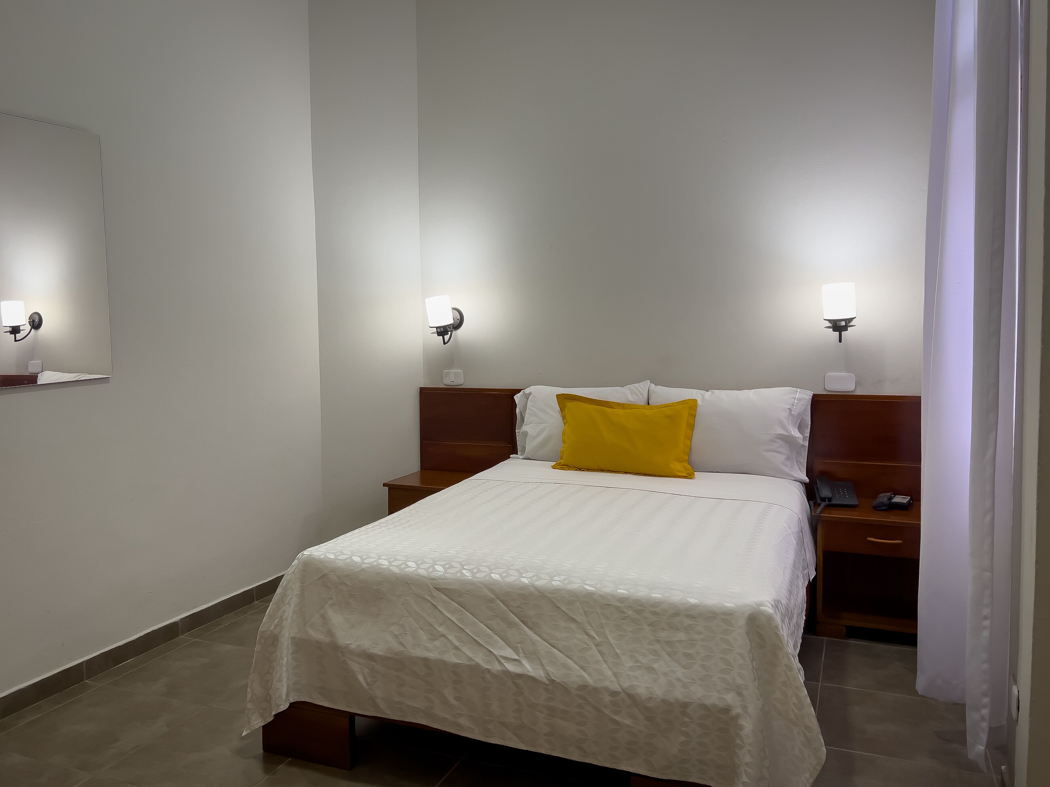 A hotel room with a bed, bedside tables, and wall-mounted lamps.