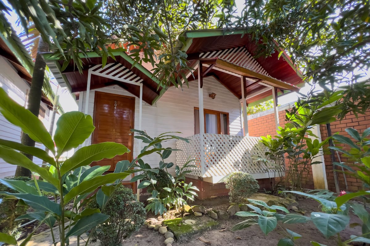 Una casa de madera con porche, rodeada de exuberante vegetación y un jardín.