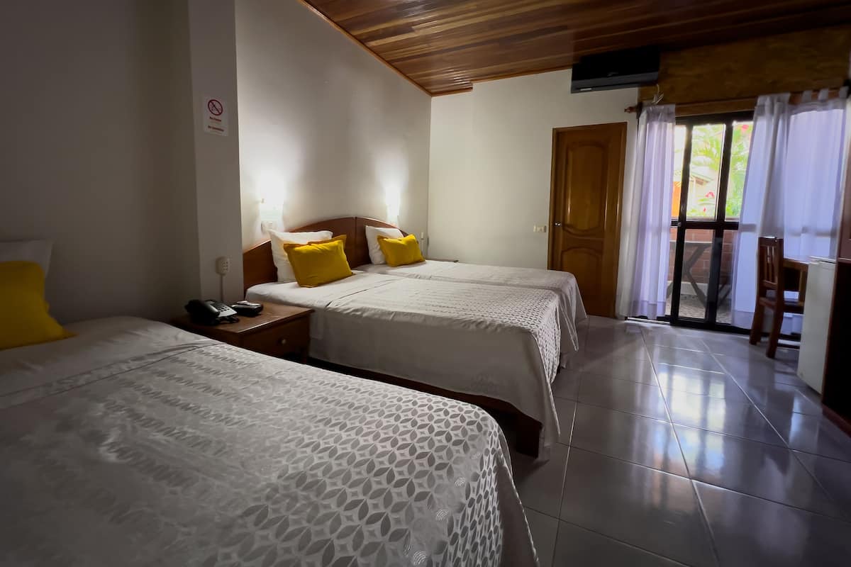 Habitación de hotel con dos camas, techo de madera, puerta que da a un balcón y suelo de baldosas.