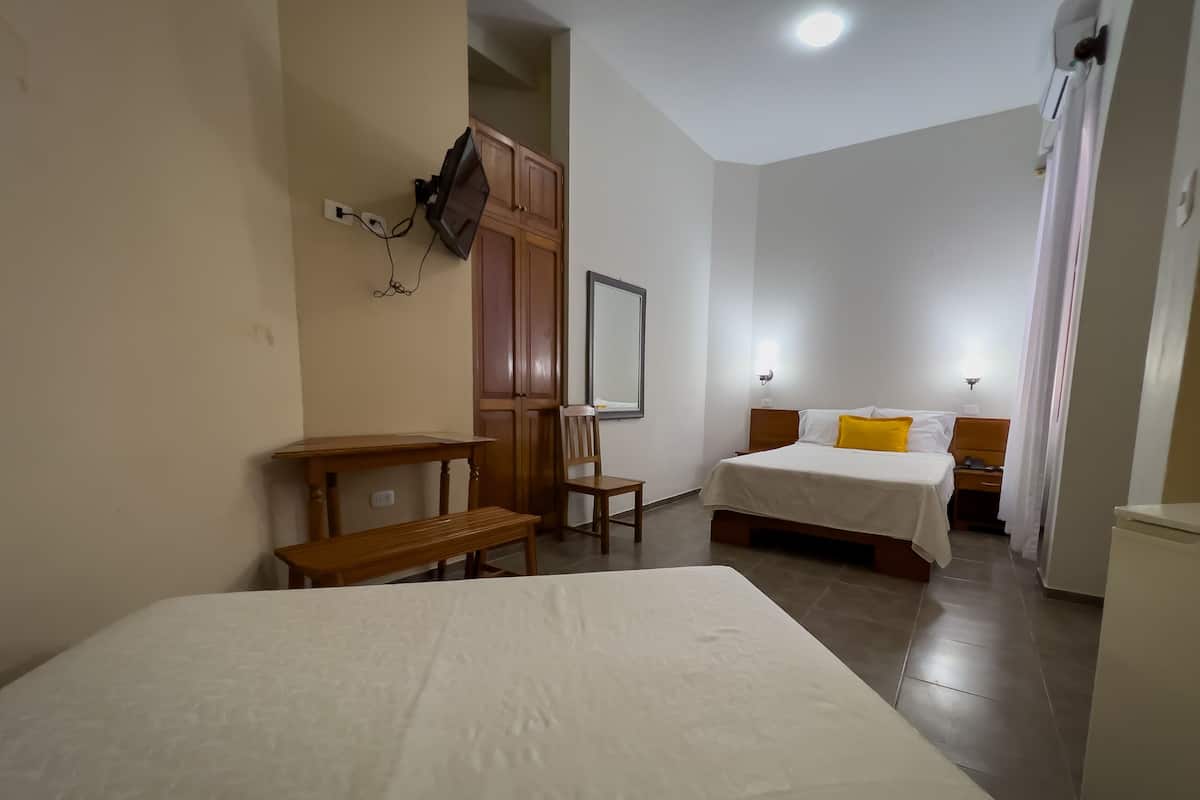 Habitación de hotel con una cama grande, una cama más pequeña, un escritorio con silla, un armario y un espejo.