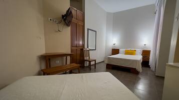 Habitación de hotel con una cama grande, una cama más pequeña, un escritorio con silla, un armario y un espejo.