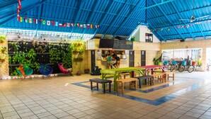 A spacious indoor area with a high ceiling, tiled floor, and several seating arrangements. There are colorful hammocks and bicycles in the background. - Wonderland Hostel By GB Collection (Cartagena)
