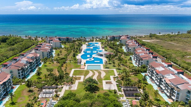 Un resort con varias edificaciones, una piscina central y vista al océano.