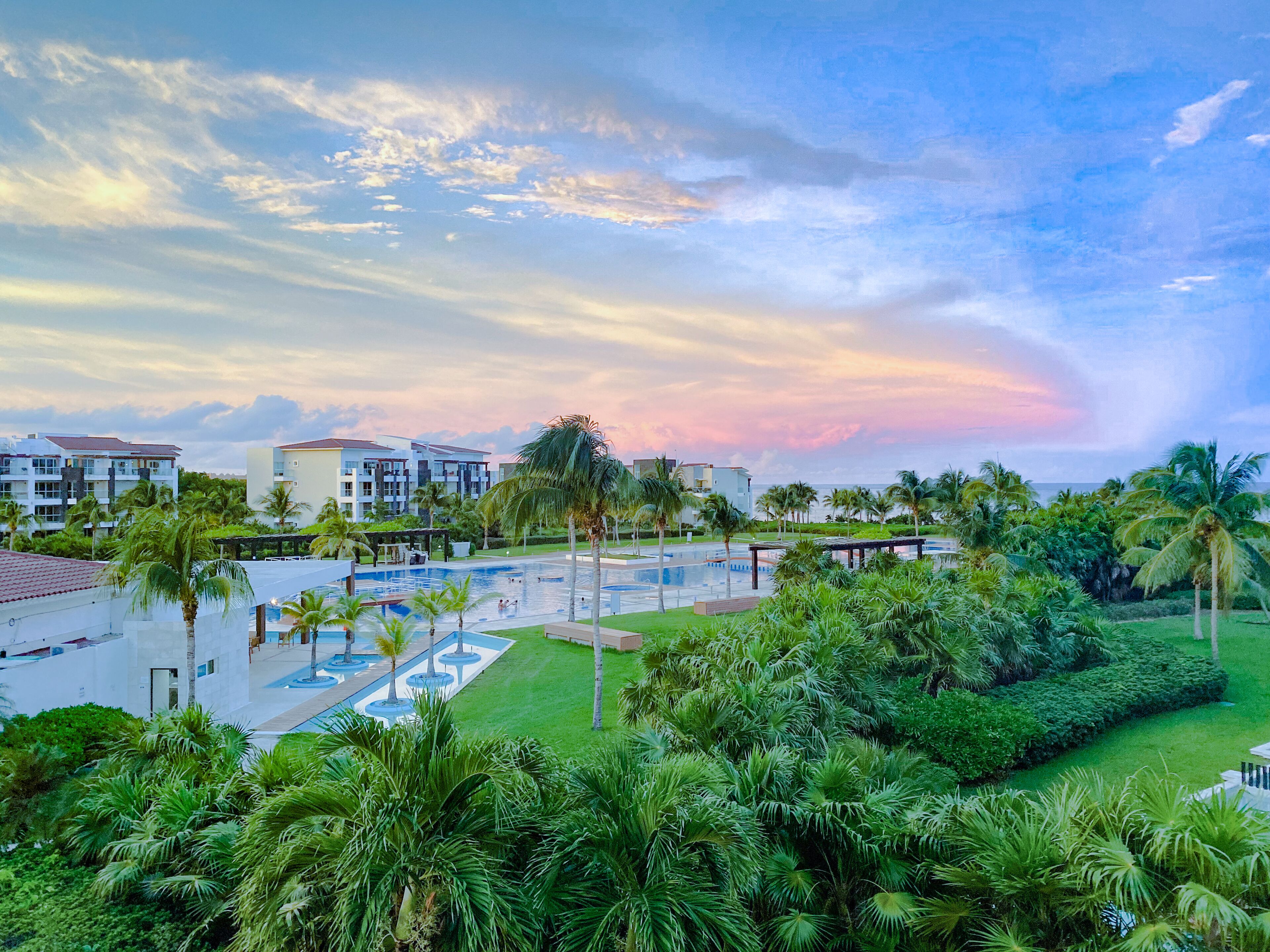 A resort with a swimming pool, palm trees, and buildings in the background.