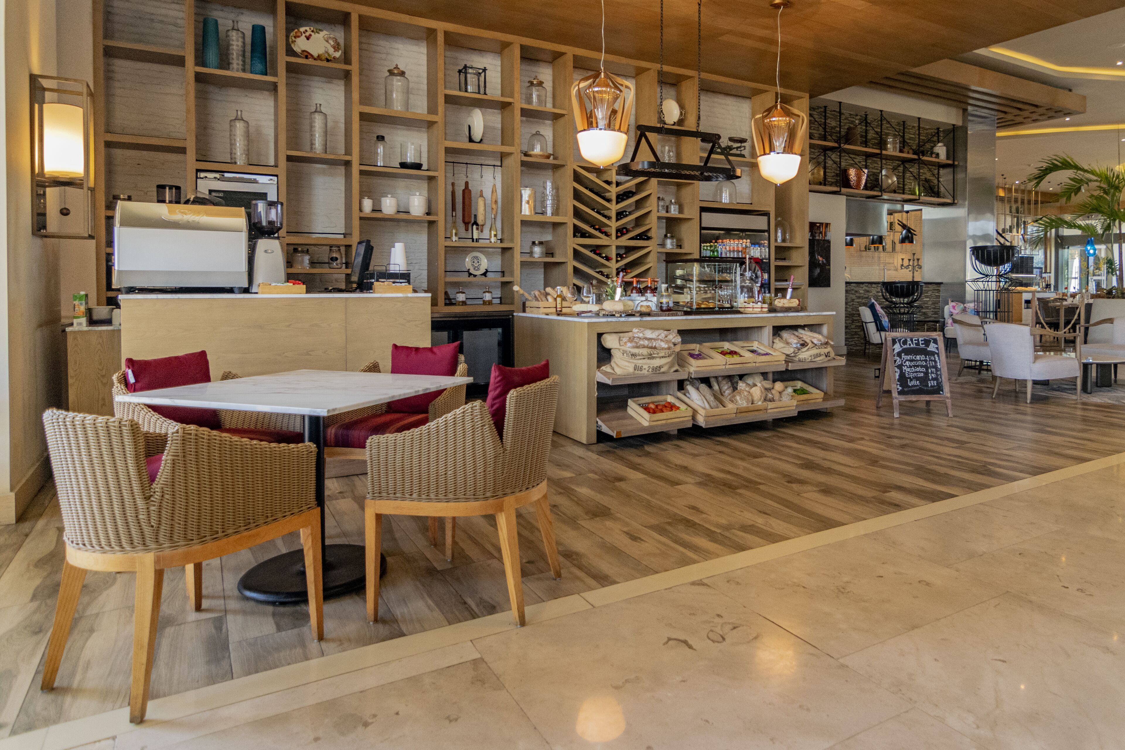 A cafe with a wooden interior, a coffee machine, wicker chairs, and shelves with various items.