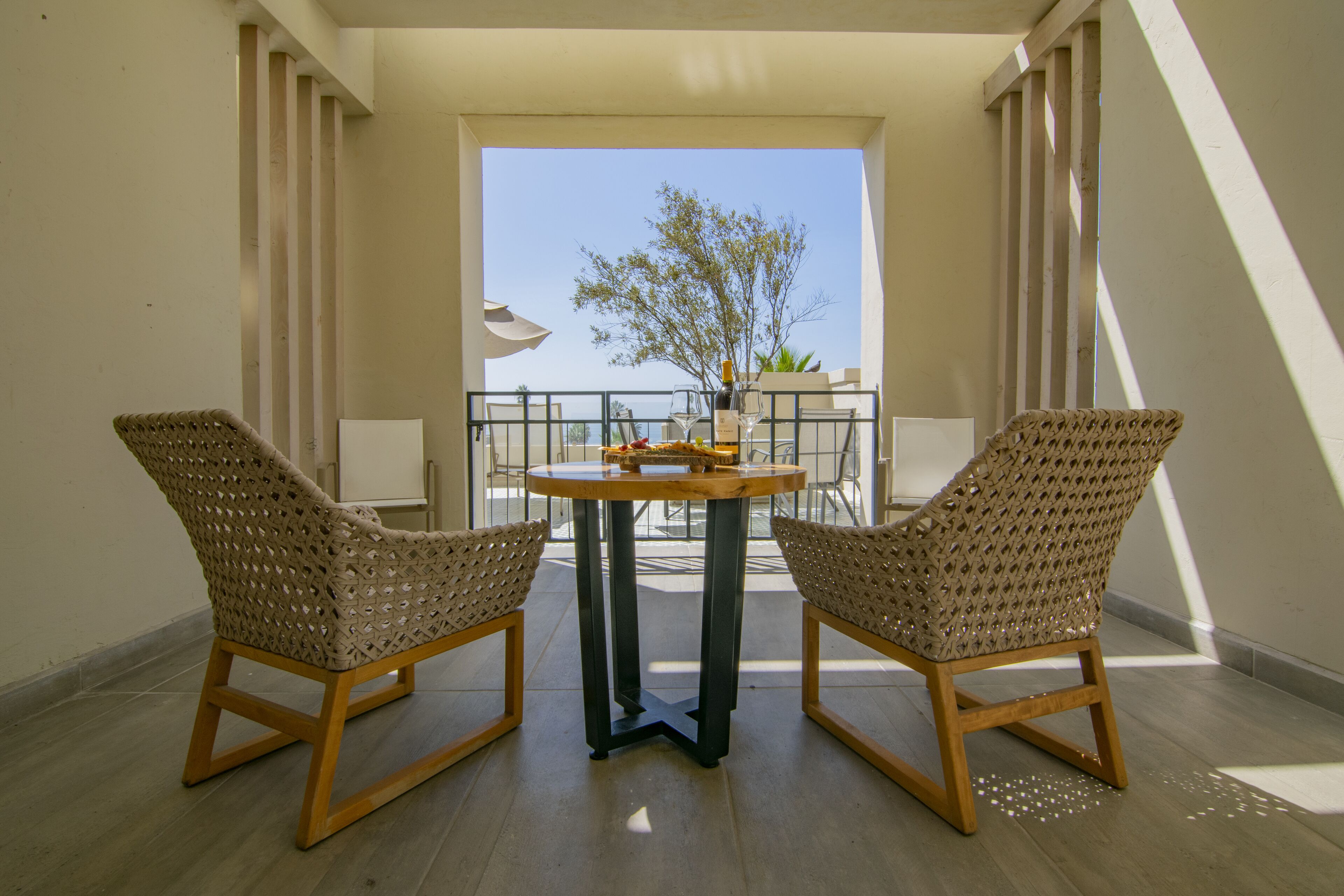 A balcony with two wicker chairs, a small round table, and a view of the sea.