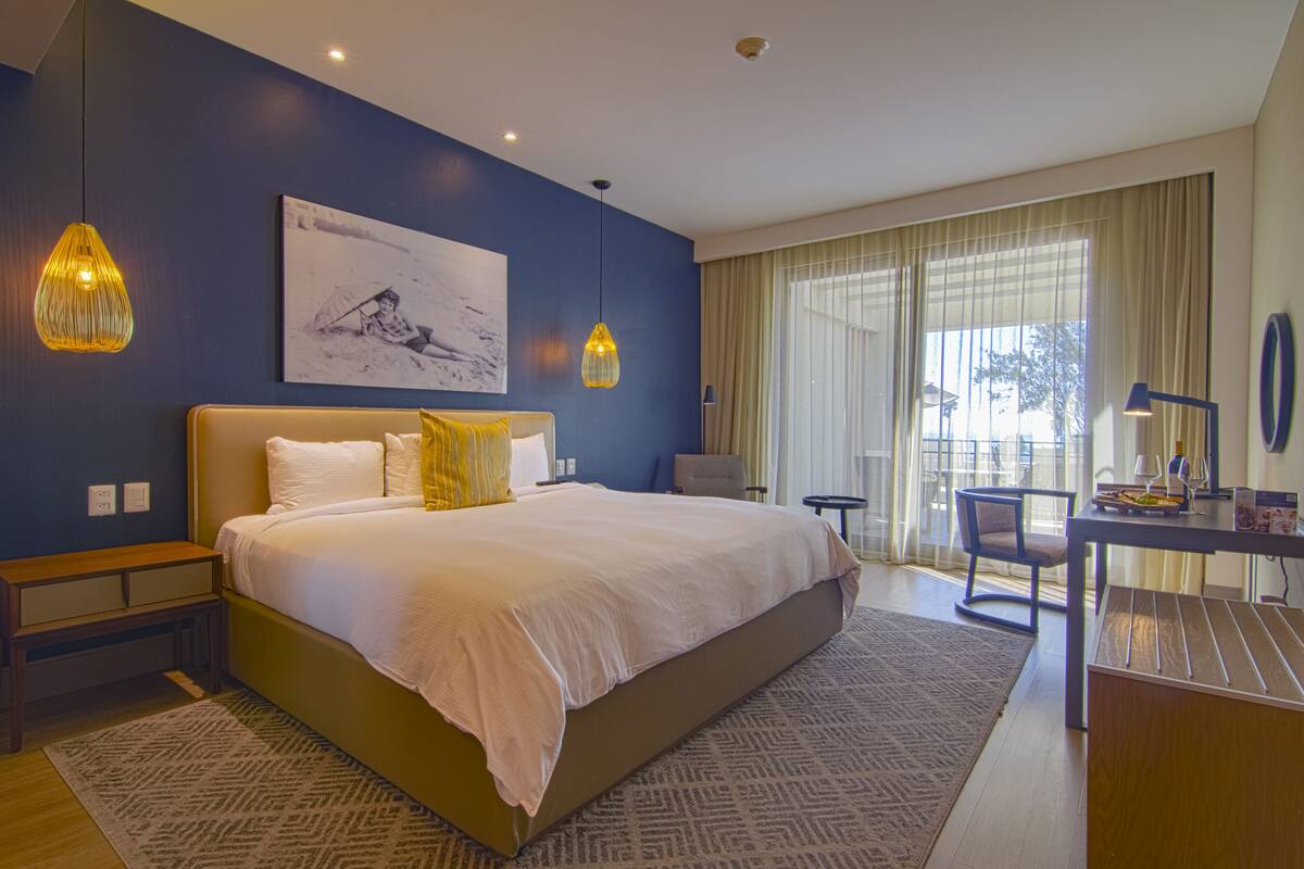 A modern hotel room with a large bed, a desk, and a view of the outdoors.
