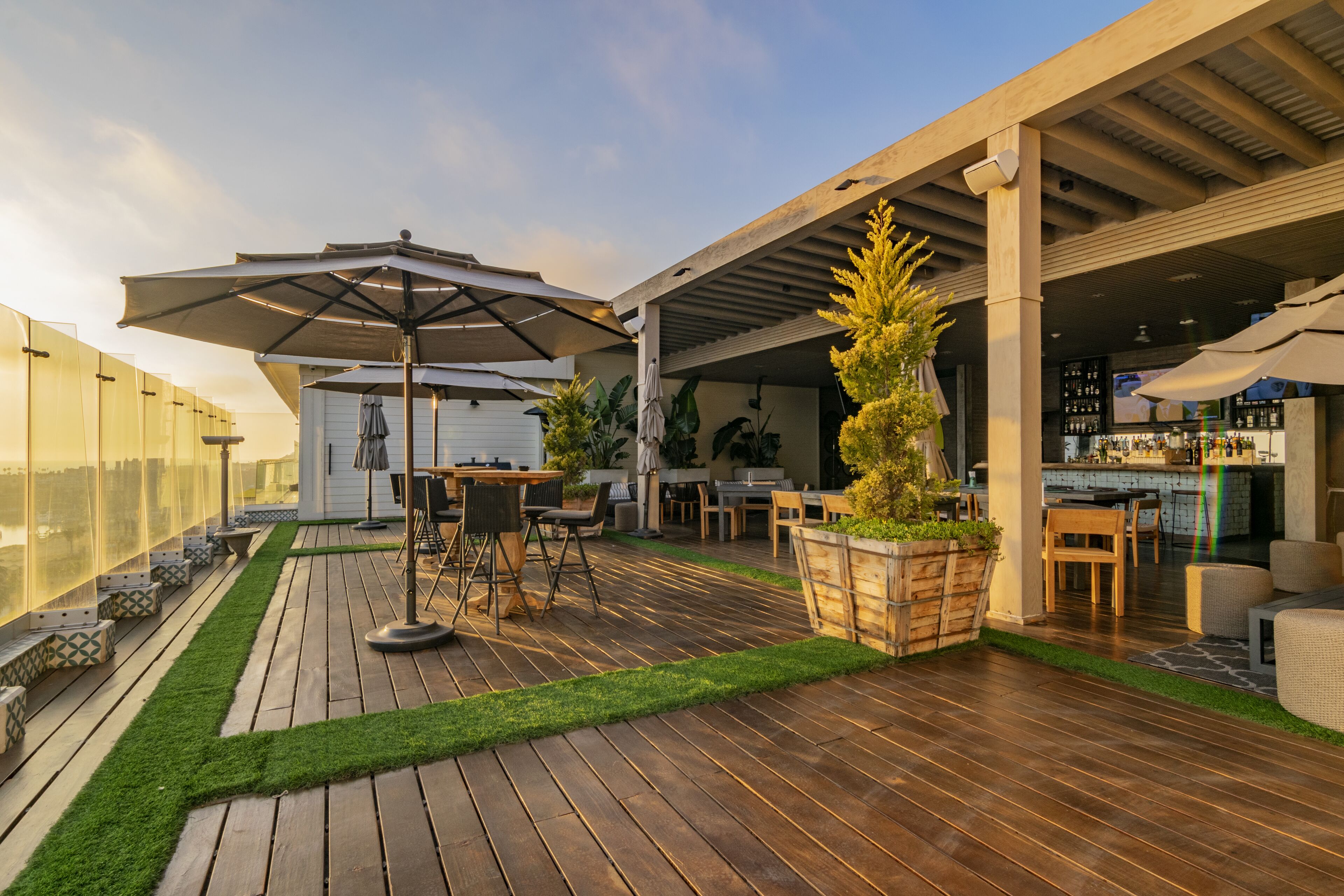 Un patio al aire libre con suelo de madera, una zona de bar y mesas para exteriores.