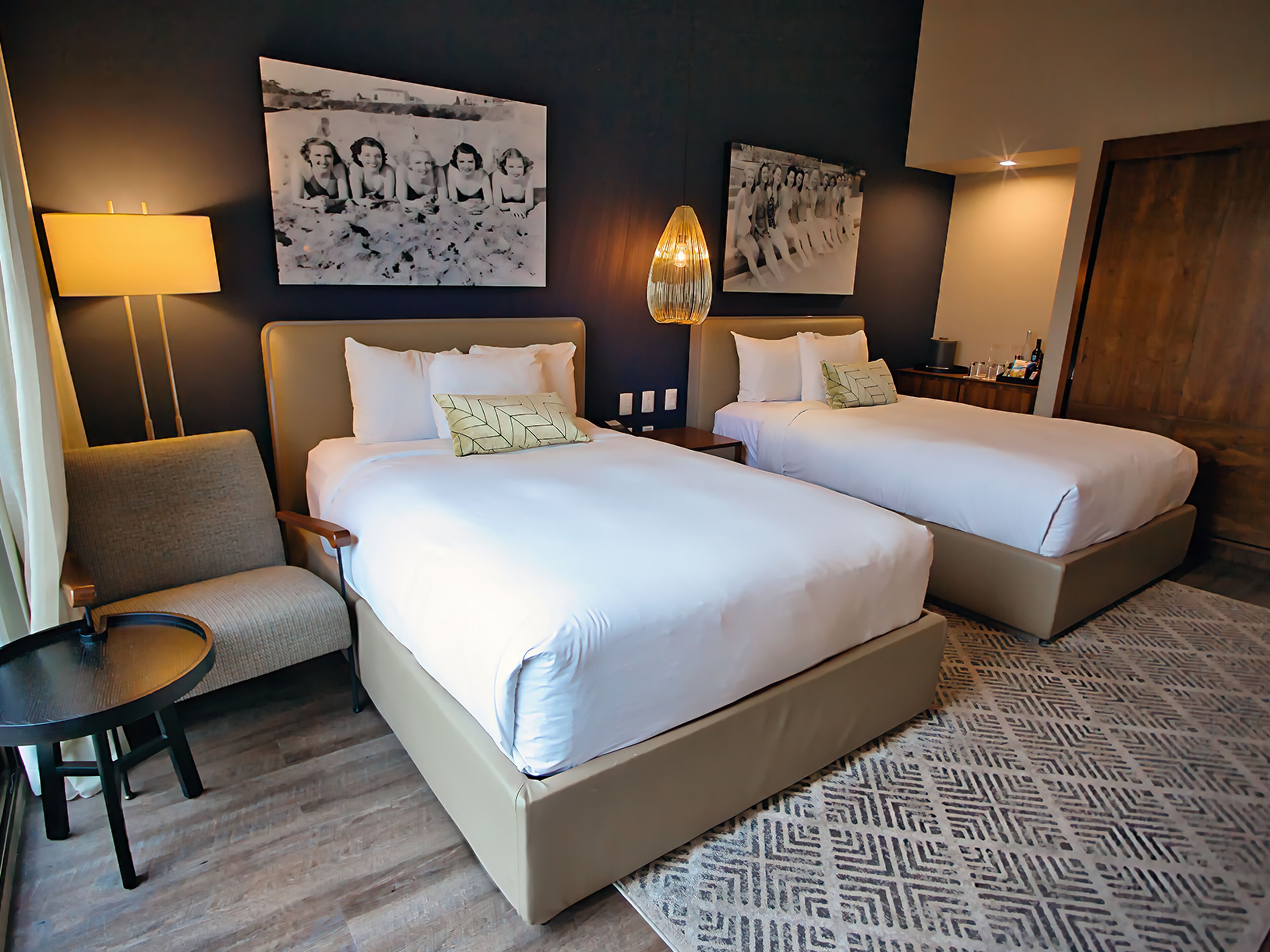 A hotel room with two beds, a sofa, a small table, and two wall-mounted lamps.