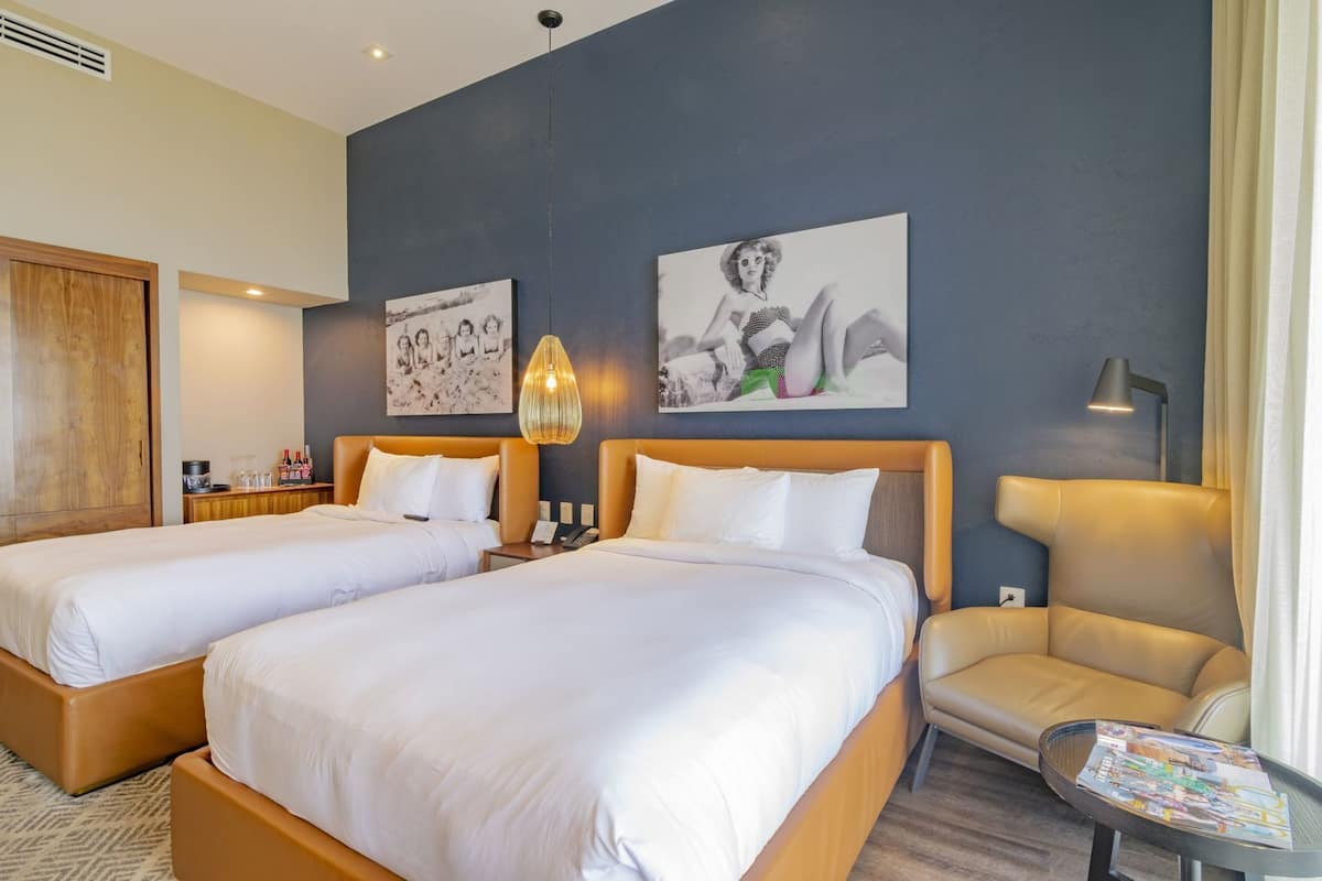 A hotel room with two beds, a sofa, a table with magazines, and artwork on the wall.
