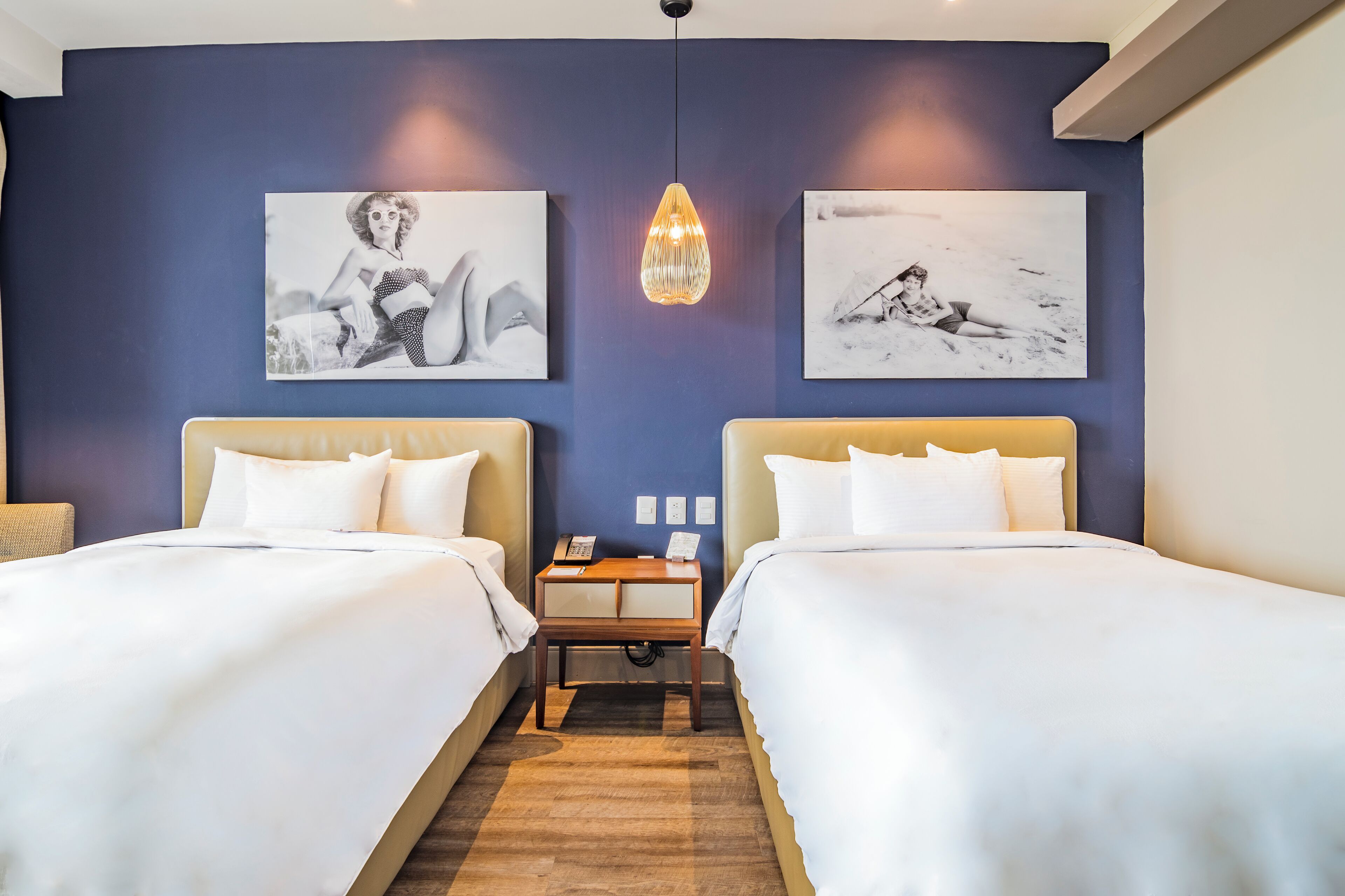 A hotel room with two beds, a wooden nightstand, and artwork on the walls.