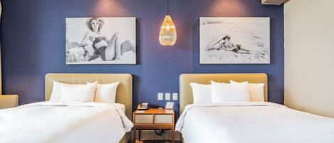 A hotel room with two beds, a wooden nightstand, and artwork on the walls.