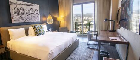 Une chambre d’hôtel avec un grand lit, un bureau, une chaise, une télévision et un balcon offrant une vue sur la ville.