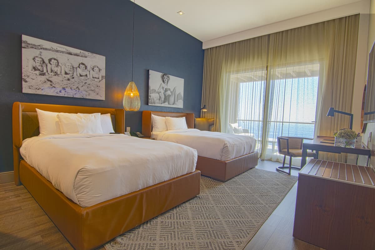 A hotel room with two beds, a desk, and a chair.