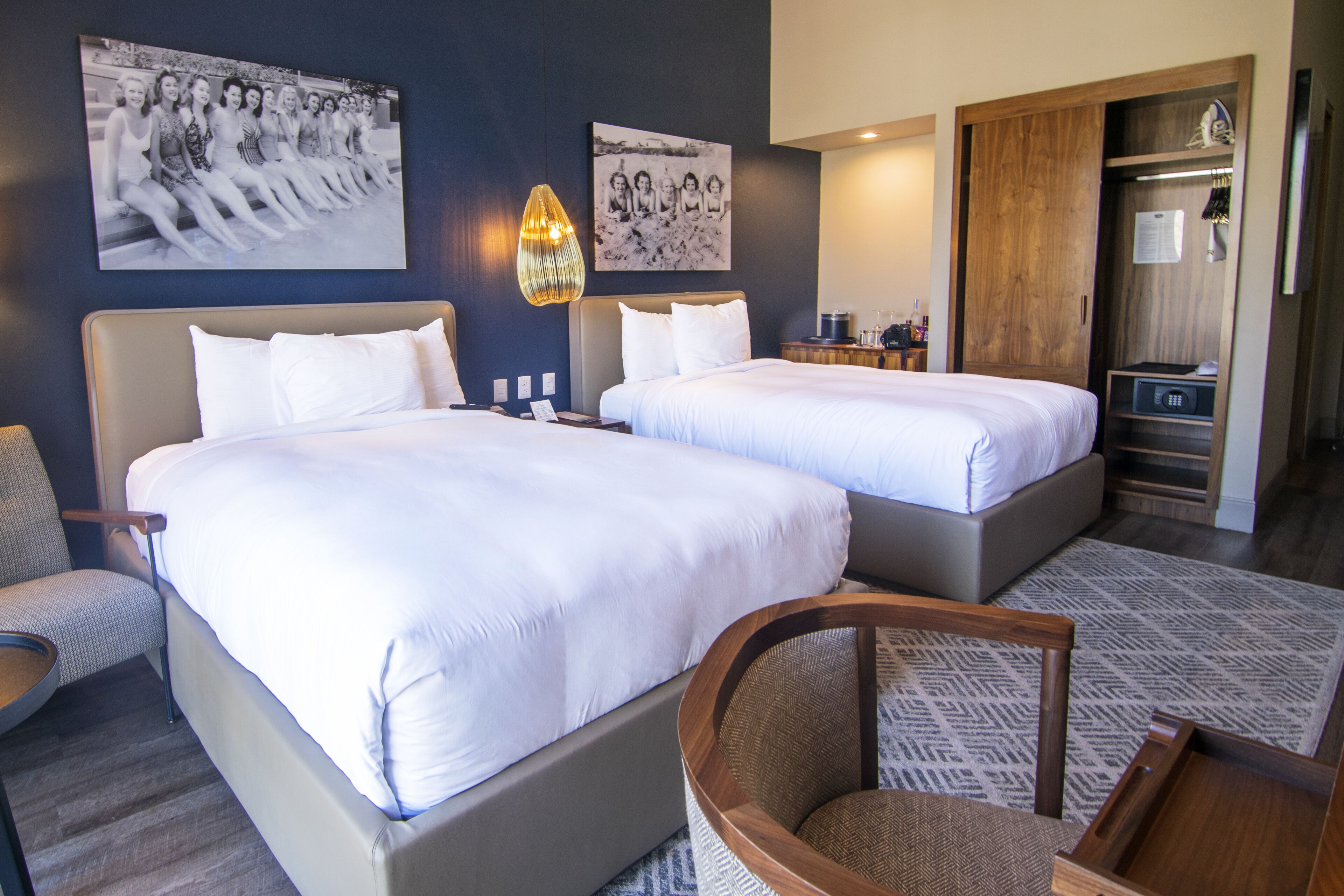 A hotel room with two beds, a chair, a desk, and a wardrobe.