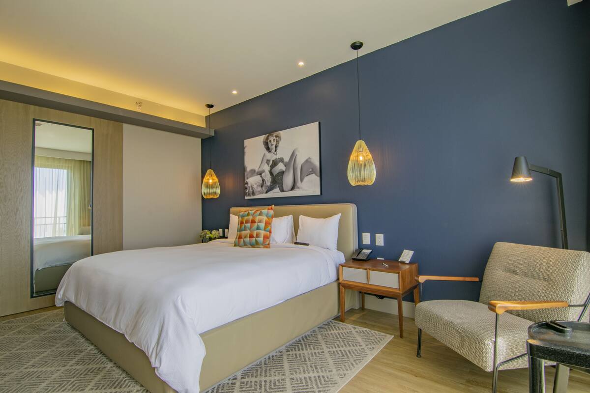 A bedroom with a large bed, bedside tables, a chair, and a painting on the wall.