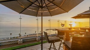 Eine Terrasse mit Meerblick, Sitzgelegenheiten im Freien und einem großen Sonnenschirm.