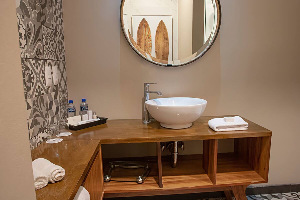A modern bathroom with a wooden vanity, a white vessel sink, and a round mirror.