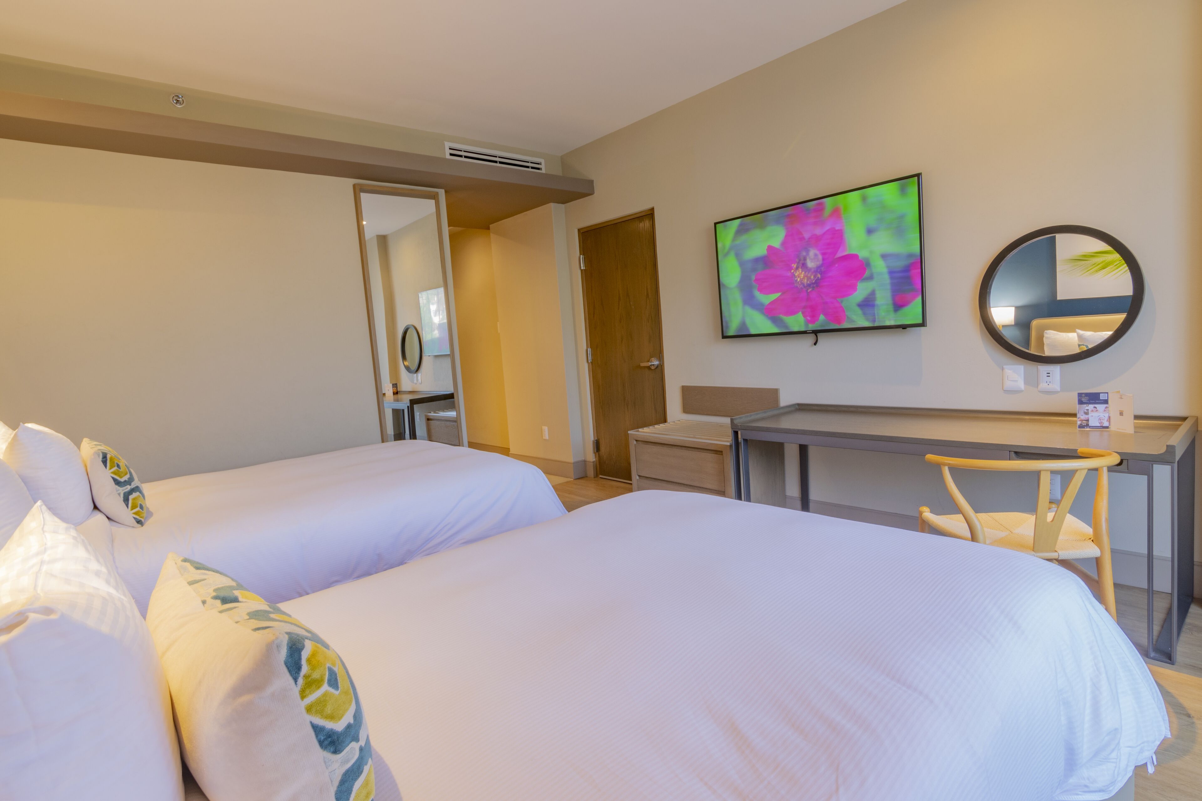 A hotel room with two beds, a desk, a chair, a TV, and a mirror.