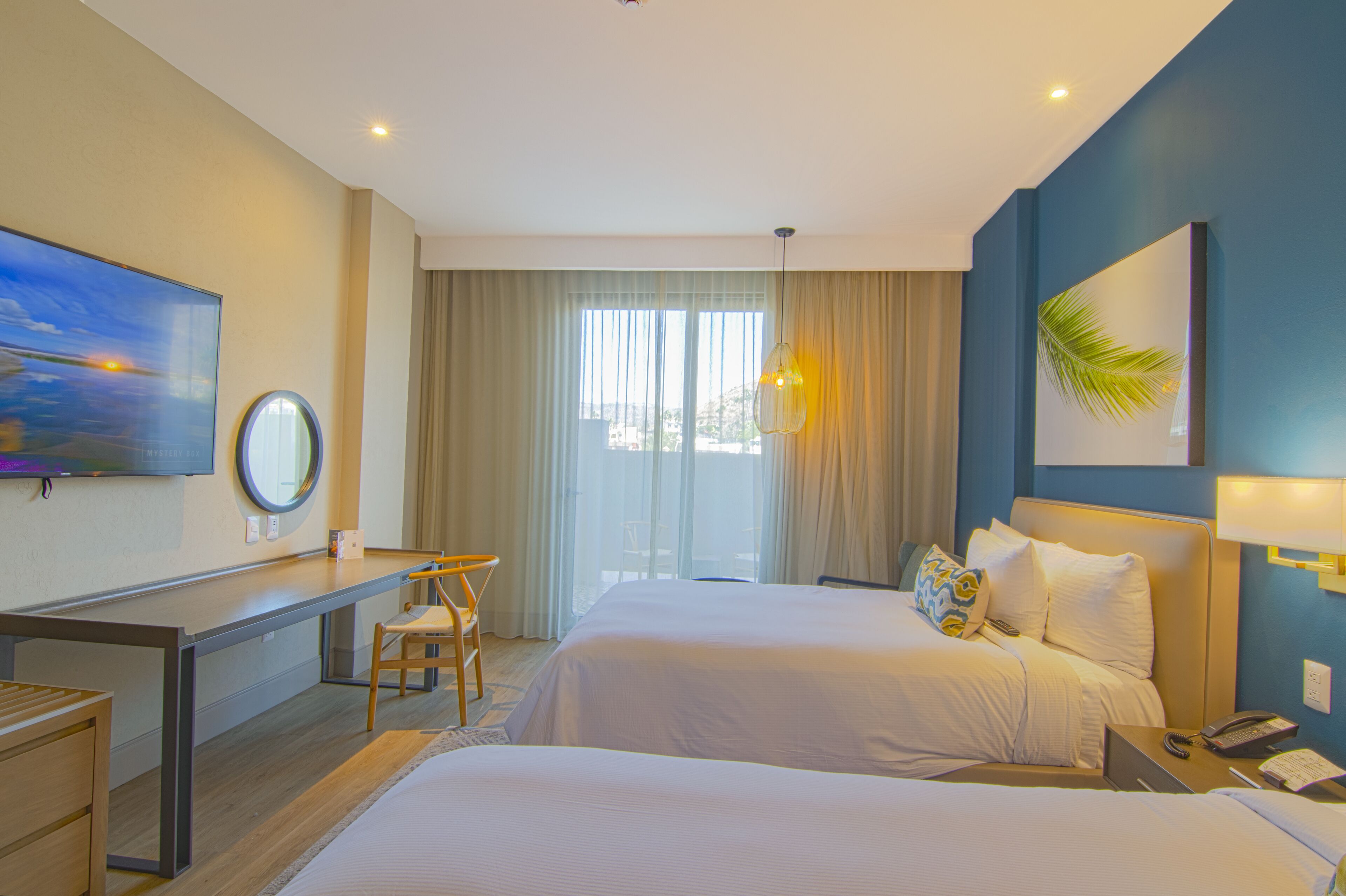 Habitación de hotel con dos camas, un escritorio y un amplio ventanal con cortinas.