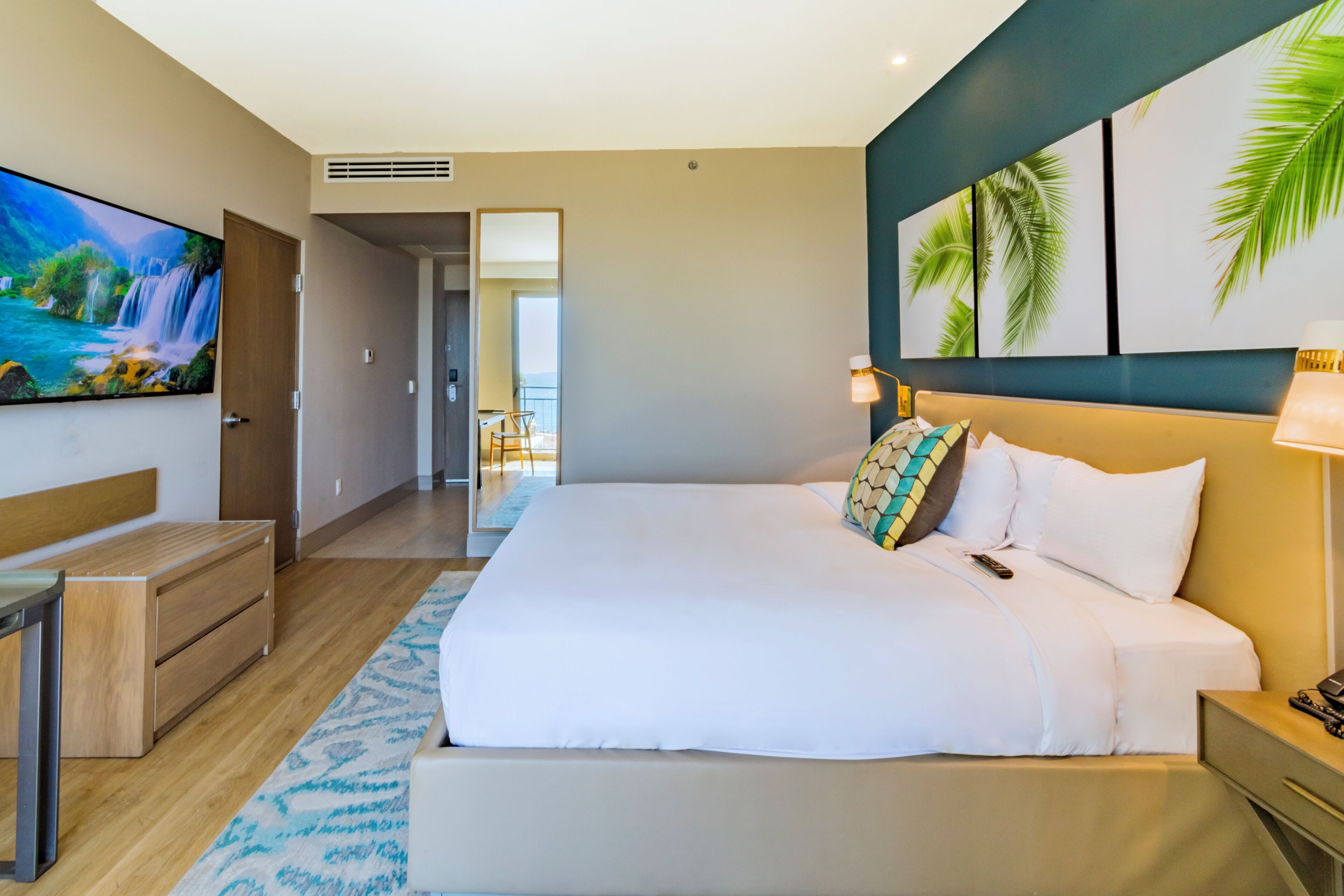 A hotel room with a large bed, a TV, a desk, and a view of the balcony.