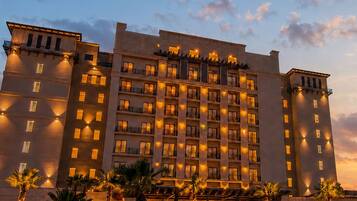 A multi-story hotel with a symmetrical facade, illuminated windows, and a landscaped front with palm trees.