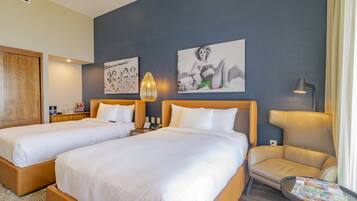 A hotel room with two beds, a chair, a table, and artwork on the wall.