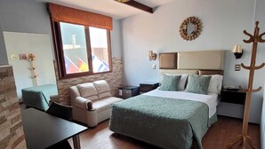 A hotel room with a bed, a sofa, a desk, a coat rack, and a window with flags. - Hotel Tinkus Inn (Lima)