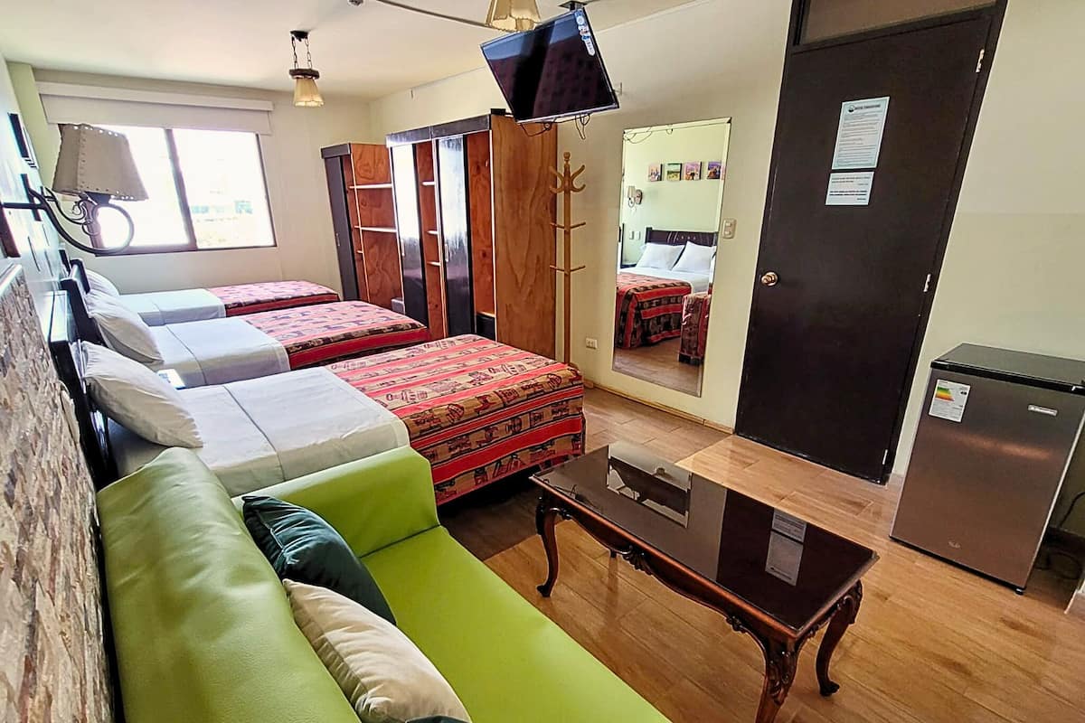 Una habitación con dos camas, un sofá verde, una mesa de madera, un espejo, un armario y un refrigerador.