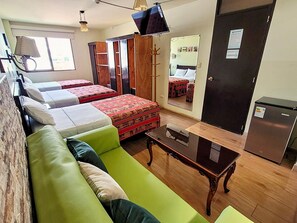 A room with two beds, a green sofa, a wooden table, a mirror, a wardrobe, and a refrigerator. - Hotel Tinkus Inn (Lima)