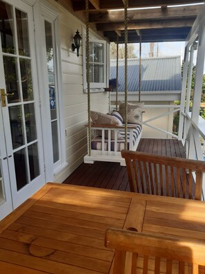 A wooden deck with a swing chair and a cushioned bench. - Harbour View Cottage B&B (Auckland)