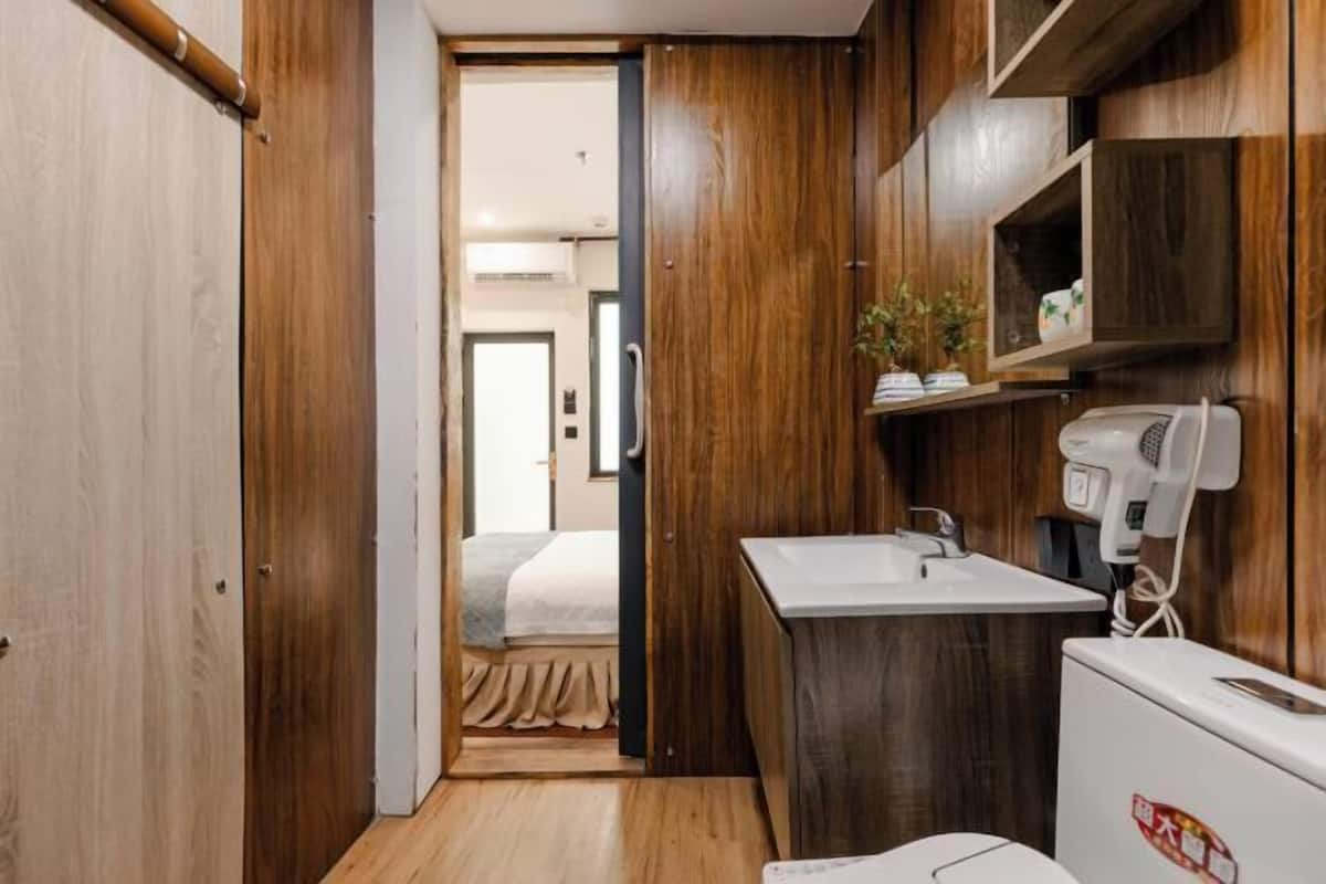 Une chambre d’hôtel de taille réduite, dotée d’une armoire en bois, d’un petit lavabo et d’un sèche-cheveux.