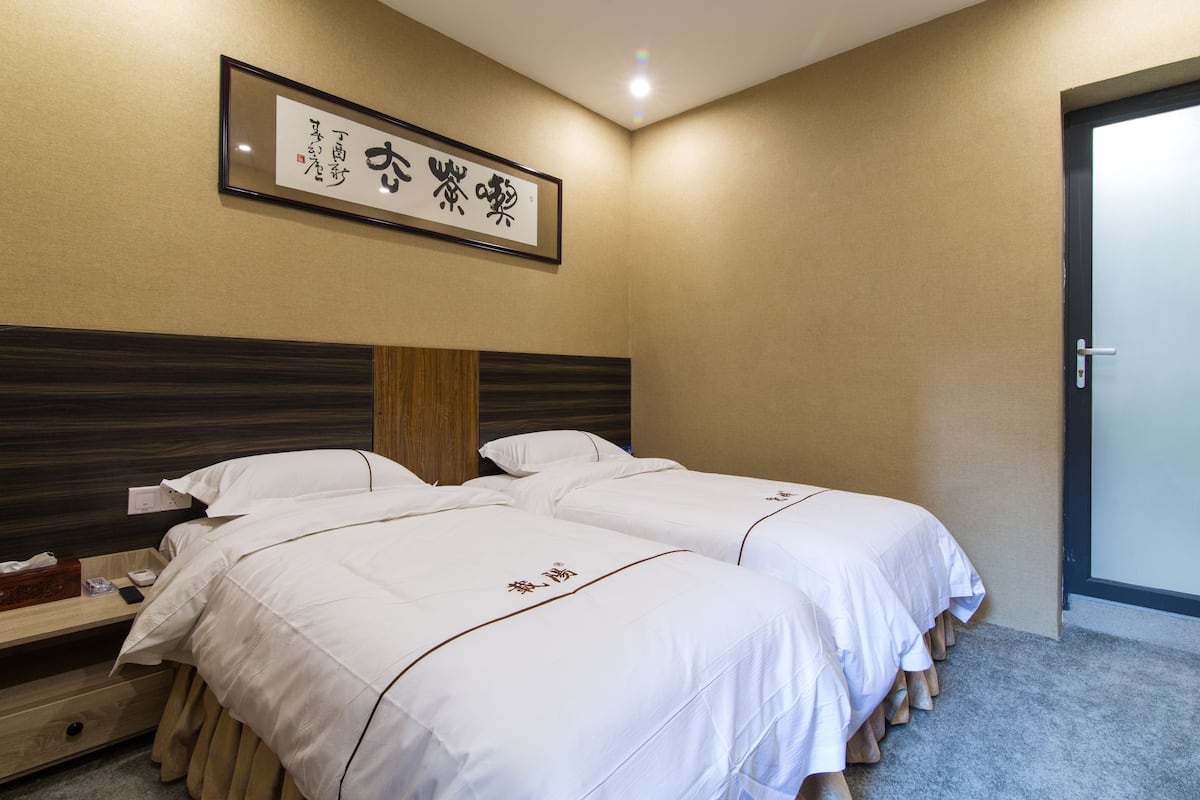Une chambre d’hôtel avec deux lits, une tête de lit en bois, une œuvre d’art encadrée au mur et une porte sur le côté droit.
