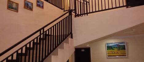 Una escalera con barandillas negras que conduce a un piso superior. Encima de la escalera, hay tres cuadros enmarcados en la pared.