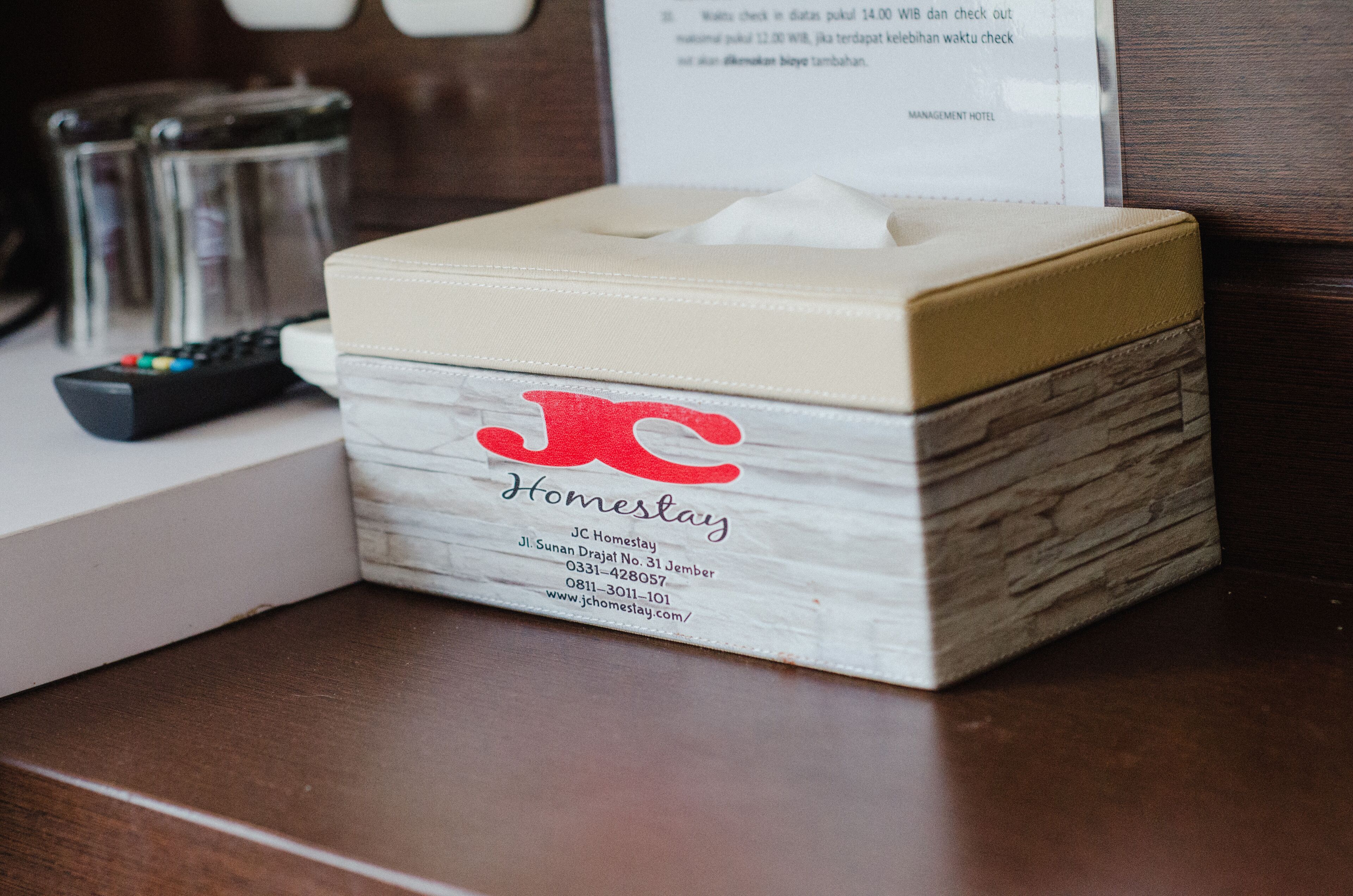 A tissue box labeled "Homestay" with contact information on a wooden surface.