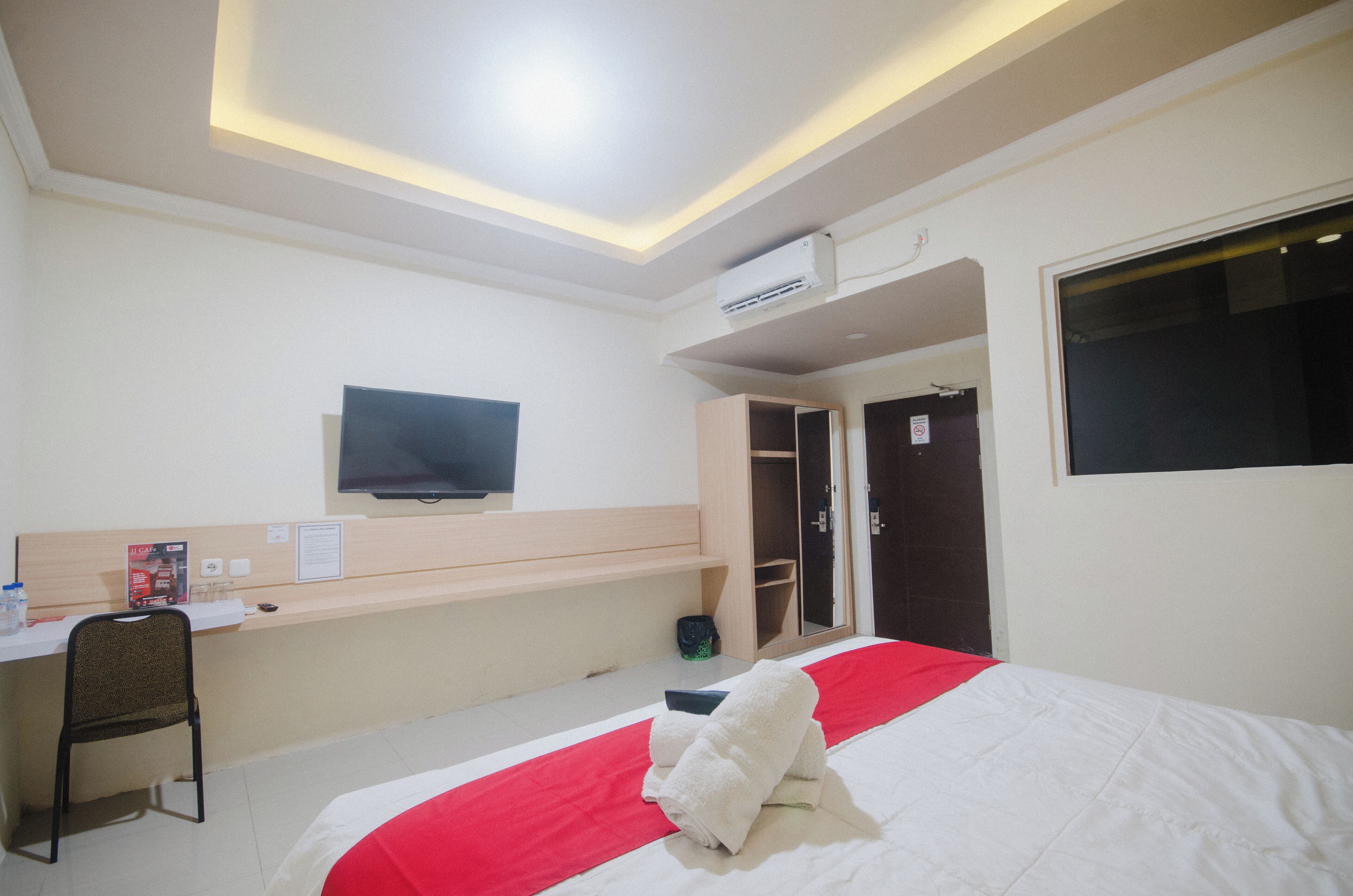 Habitación de hotel con cama, escritorio, silla, televisor y armario.