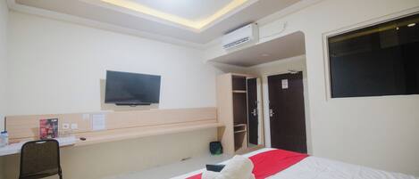 Habitación de hotel con cama, escritorio, silla, televisor y armario.
