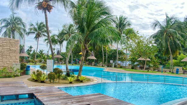 A swimming pool with wooden deck areas, surrounded by palm trees and tropical plants. - Panoramic 180 Cozy Suite by D Imperio Homestay (George Town)
