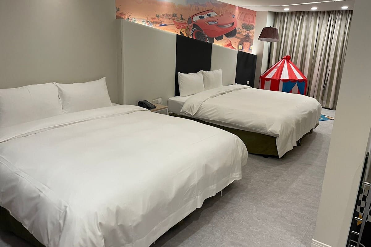 A hotel room with two beds, a mural of a cartoon car on the wall, a lamp, and a striped curtain.